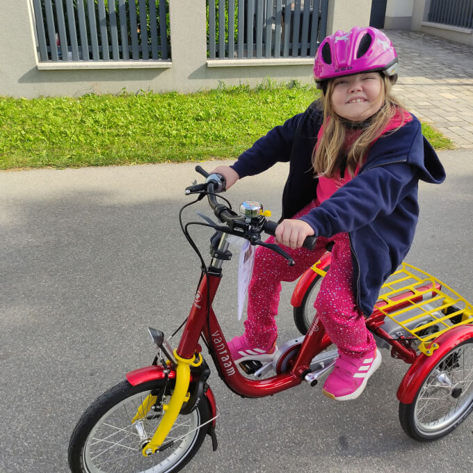 Foto: Carmen fährt auf der Straße vor dem Haus auf ihrem neuen Therapiefahrrad